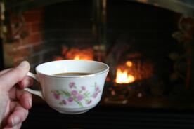 A person is holding a cup of tea in front of a fireplace.